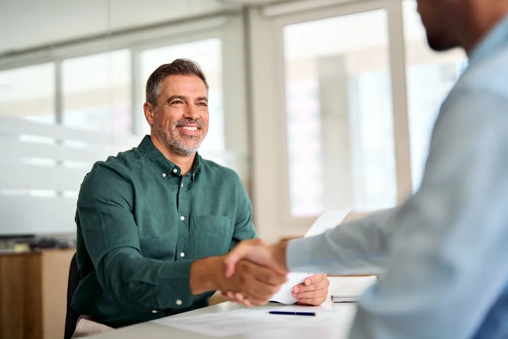 Smiling middle aged business man handshaking partner making partnership collaboration agreement at office meeting,